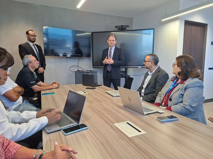 A meeting around a conference table with a presenter standing at the front